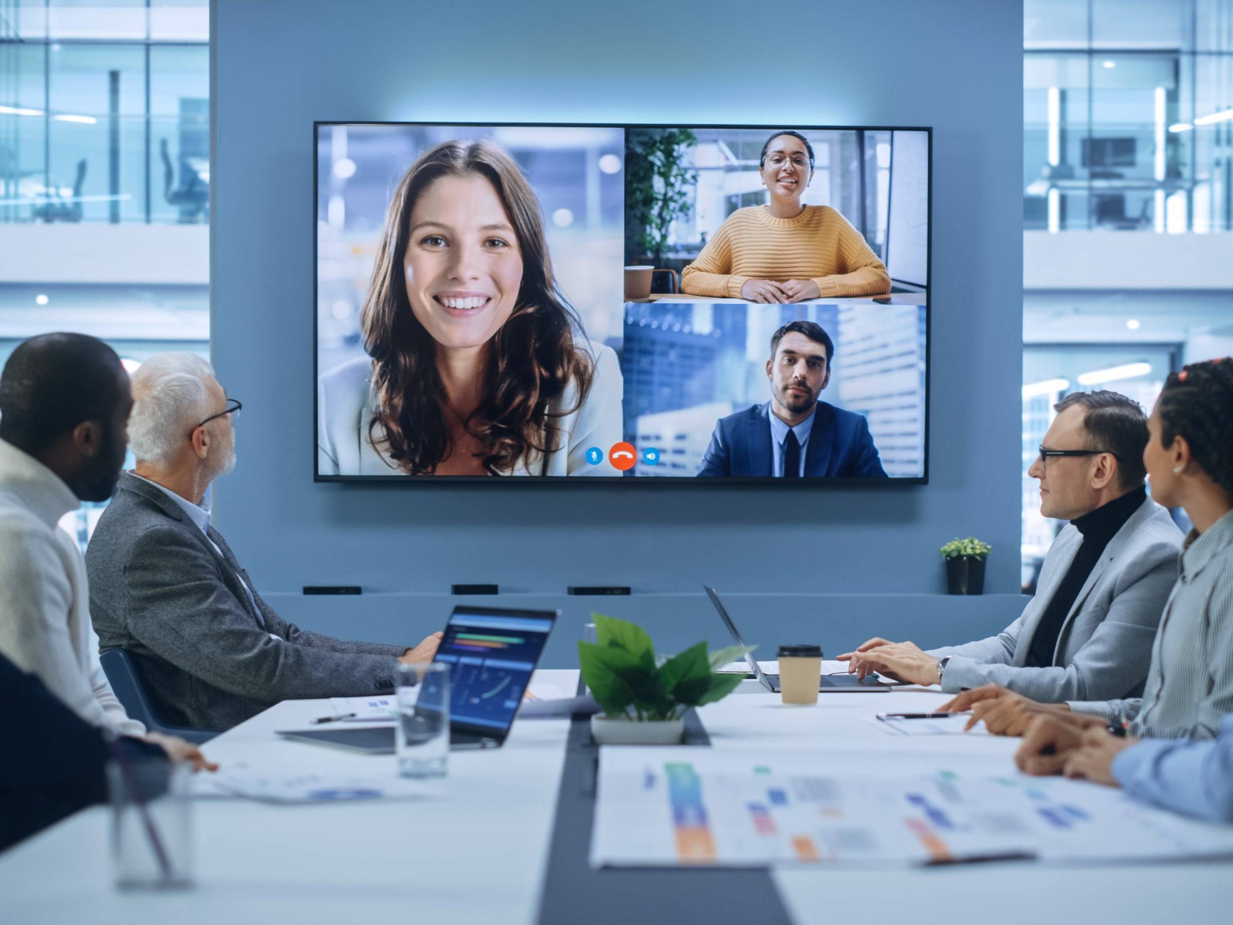 People having a hybrid meeting on a boardroom along with a digital led screen where some members are physically present and others joined virtually.